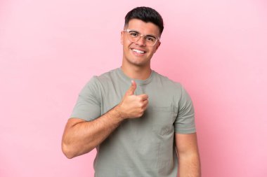 Pembe arka planda izole edilmiş beyaz, yakışıklı bir genç baş parmak hareketi yapıyor.