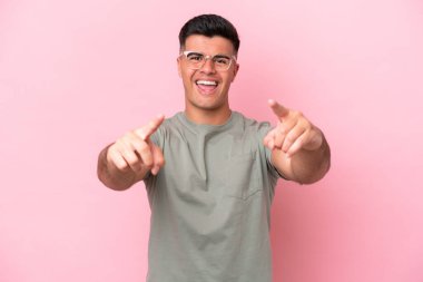 Pembe arka planda izole edilmiş beyaz, yakışıklı genç adam şaşırmış ve ön tarafı işaret ediyor.