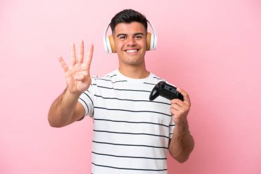 Young handsome man playing with a video game controller isolated on pink background happy and counting four with fingers