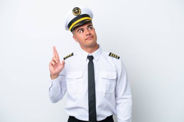 Airplane pilot caucasian man isolated on white background with fingers crossing and wishing the best