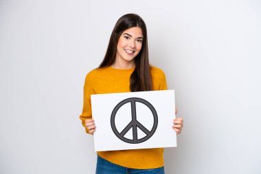 Young Brazilian woman isolated on white background holding a placard with peace symbol with happy expression