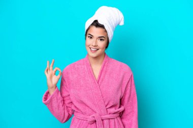 Young Brazilian woman with a bathrobe isolated on blue background showing ok sign with fingers