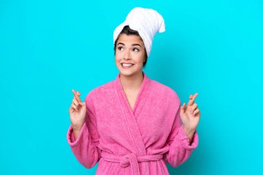 Young Brazilian woman with a bathrobe isolated on blue background with fingers crossing