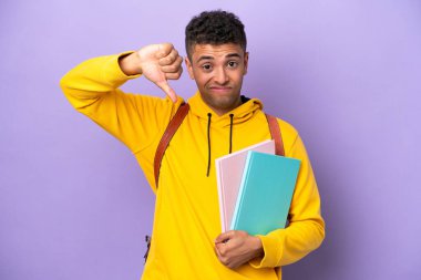 Young student Brazilian man isolated on purple background showing thumb down with negative expression