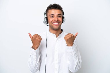 Telemarketer Brazilian man working with a headset isolated on white background with thumbs up gesture and smiling