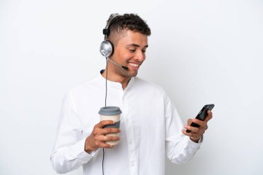 Tele pazarlamacı Brezilyalı adam beyaz arka planda izole edilmiş bir kulaklıkla çalışıyor. Elinde kahve ve cep telefonu var.