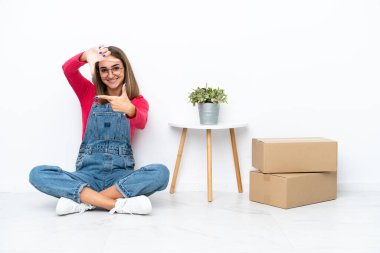 Young caucasian woman sitting on the floor among boxes focusing face. Framing symbol