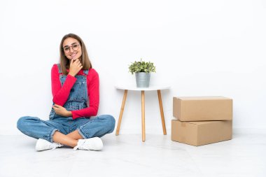 Young caucasian woman sitting on the floor among boxes with glasses and smiling