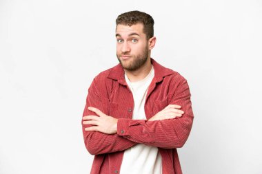 Genç, sarışın, soyutlanmış beyaz arka planda, omuzlarını kaldırırken şüpheyle hareket eden bir adam.