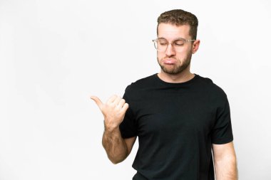 Young handsome blonde man over isolated white background unhappy and pointing to the side