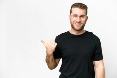 Soyutlanmış beyaz arka planı olan yakışıklı sarışın genç bir adam bir ürün sunmak için kenarı işaret ediyor.