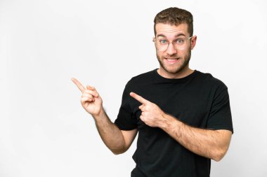 Young handsome blonde man over isolated white background frightened and pointing to the side