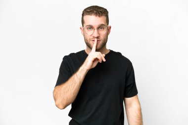 Soyutlanmış beyaz arka planda genç, yakışıklı sarışın bir adam sessizlik işareti gösteriyor. Parmağını ağzına sokuyor.