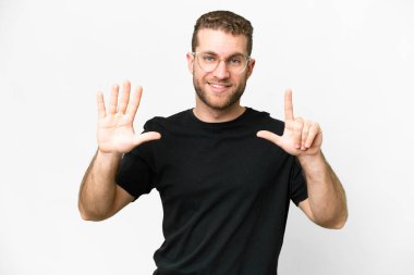 Genç yakışıklı sarışın adam izole edilmiş beyaz arka planda yediyi parmaklarıyla sayıyor.