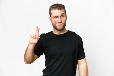 Young handsome blonde man over isolated white background with fingers crossing and wishing the best