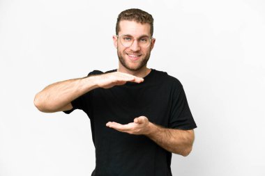 Young handsome blonde man over isolated white background holding copyspace imaginary on the palm to insert an ad