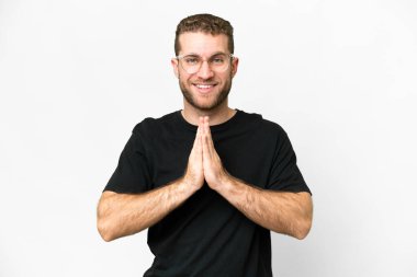 Young handsome blonde man over isolated white background keeps palm together. Person asks for something