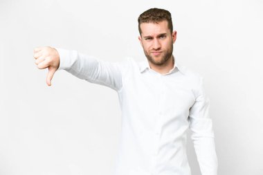 Soyutlanmış beyaz arka planda genç, yakışıklı sarışın bir adam olumsuz bir ifadeyle baş parmağını aşağı gösteriyor.