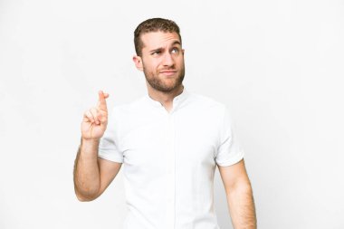 Young handsome blonde man over isolated white background with fingers crossing and wishing the best