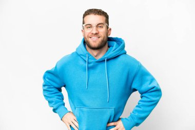 Young handsome blonde man over isolated white background posing with arms at hip and smiling