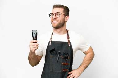 Barber man in an apron over isolated white background posing with arms at hip and smiling