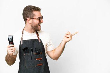 Barber man in an apron over isolated white background pointing finger to the side and presenting a product