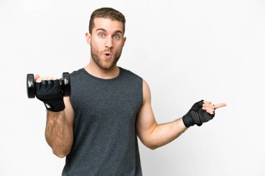 Young sport man making weightlifting over isolated white background surprised and pointing side