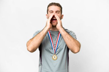 Young handsome blonde man with medals over isolated white background shouting and announcing something