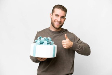 Young handsome blonde man with a big cake over isolated white background giving a thumbs up gesture