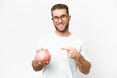 Young handsome blonde man holding a piggybank and pointing it