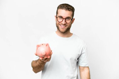 Young handsome blonde man holding a piggybank with happy expression
