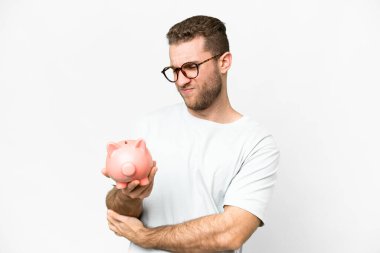 Young handsome blonde man holding a piggybank with sad expression