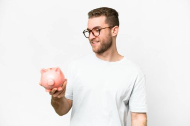 Young handsome blonde man holding a piggybank with happy expression