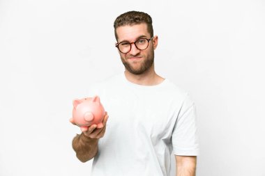 Young handsome blonde man holding a piggybank with sad expression
