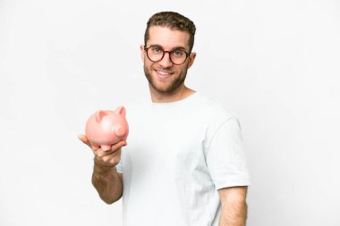 Young handsome blonde man holding a piggybank smiling a lot