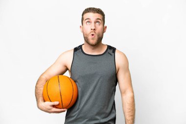 Handsome young man playing basketball over isolated white background looking up and with surprised expression