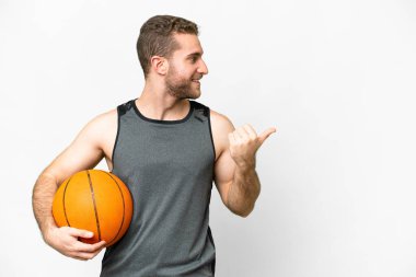Handsome young man playing basketball over isolated white background pointing to the side to present a product