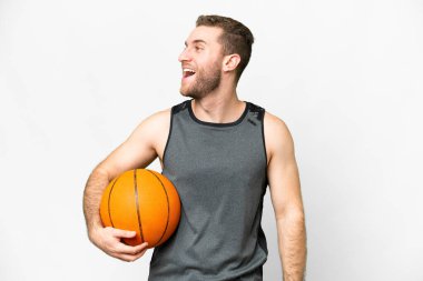Handsome young man playing basketball over isolated white background laughing in lateral position