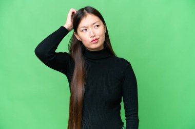 Young Asian woman over isolated chroma key background having doubts while scratching head