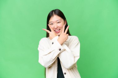 Genç Asyalı kadın izole edilmiş krom anahtar arka planda gülümsüyor ve zafer işareti gösteriyor