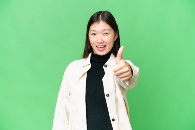 Young Asian woman over isolated chroma key background with thumbs up because something good has happened