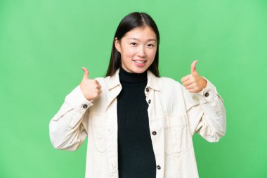 Soyutlanmış krom anahtar geçmişi olan genç Asyalı bir kadın baş parmak hareketi yapıyor.