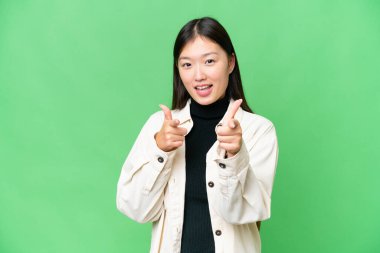 Young Asian woman over isolated chroma key background pointing to the front and smiling