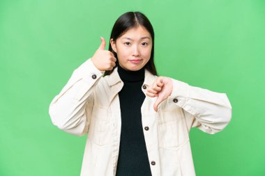 Young Asian woman over isolated chroma key background making good-bad sign. Undecided between yes or not