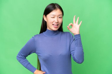 Young Asian woman over isolated chroma key background showing ok sign with fingers