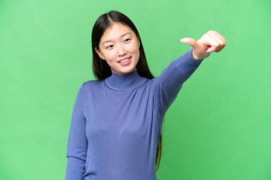 Soyutlanmış krom anahtar geçmişi olan genç Asyalı bir kadın baş parmak hareketi yapıyor.