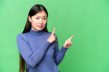 Young Asian woman over isolated chroma key background frightened and pointing to the side