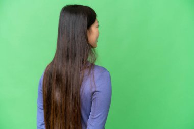 Young Asian woman over isolated chroma key background in back position and looking back