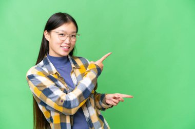 Young Asian woman over isolated chroma key background pointing finger to the side and presenting a product