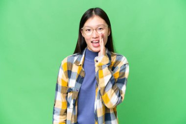 Young Asian woman over isolated chroma key background shouting with mouth wide open